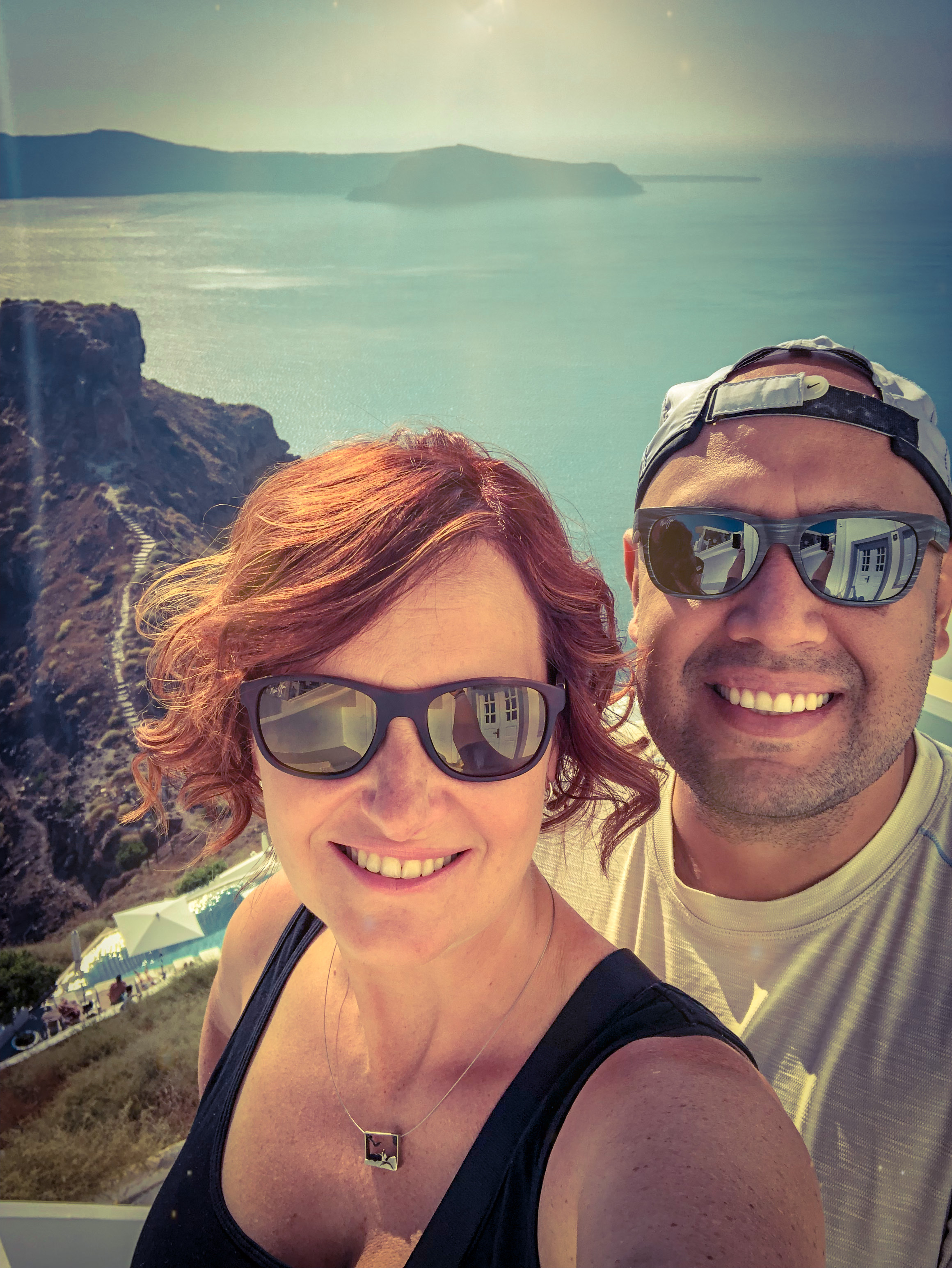 Armando and Tamara in Santorini, Greece with a view of Skaros Rock and the Aegean Sea in the background.